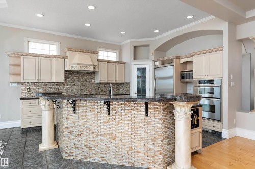 Kitchen featuring an island with stone mosaic facade and decorative columns, stainless steel appliances, a tile backsplash, light-colored cabinetry, and recessed lighting - 16103 89 Street, Edmonton, AB - Indoor Photo Showing Kitchen With Upgraded Kitchen