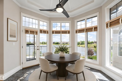 Bay window dining area featuring extensive glazing, a white patio door with a black metal railing, a modern ceiling fan, and intricate flooring with dark and light tile accents - 16103 89 Street, Edmonton, AB - Indoor Photo Showing Dining Room