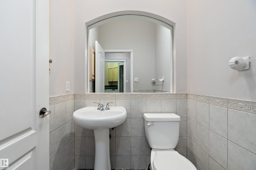 Bathroom featuring a pedestal sink, a white toilet, and light-toned ceramic tile wainscoting with a decorative border - 16103 89 Street, Edmonton, AB - Indoor Photo Showing Bathroom