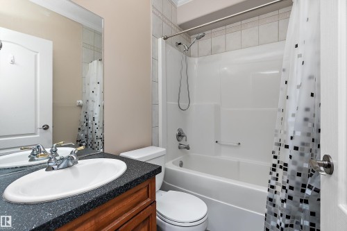 Bathroom featuring a white vanity sink, dark countertop, wood-finish cabinetry, and a full-size bathtub with a shower - 16103 89 Street, Edmonton, AB - Indoor Photo Showing Bathroom