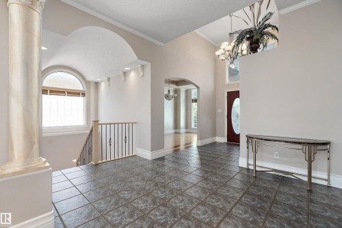 Foyer featuring dark grey tile flooring, a decorative column, an arched window with blinds, a staircase with a wood handrail and wrought iron balusters, and a red entry door with decorative glass - 16103 89 Street, Edmonton, AB - Indoor Photo Showing Other Room