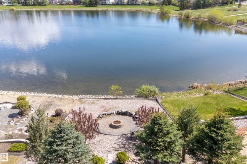 Waterfront property featuring a circular paver patio with a built-in fire pit, surrounded by mature evergreen trees and decorative landscaping - 16103 89 Street, Edmonton, AB - Outdoor With Body Of Water With View