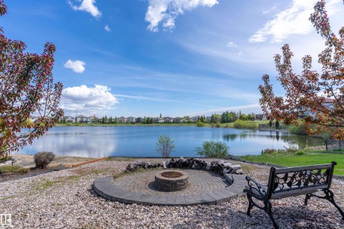 Waterside property featuring a circular paver fire pit with a stone surround, gravel ground cover, and mature trees - 16103 89 Street, Edmonton, AB - Outdoor With Body Of Water With View