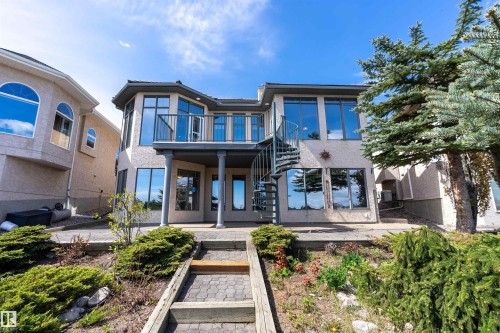 Multi-level exterior featuring a spiral staircase, expansive windows, a second-story balcony, and a ground-level patio with stone pavers - 16103 89 Street, Edmonton, AB - Outdoor With Facade