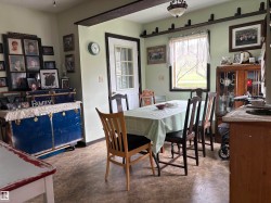 Dining area featuring a central window, light green walls, a white exterior door with glass panes, wood-finish flooring, and a decorative ceiling beam. - 