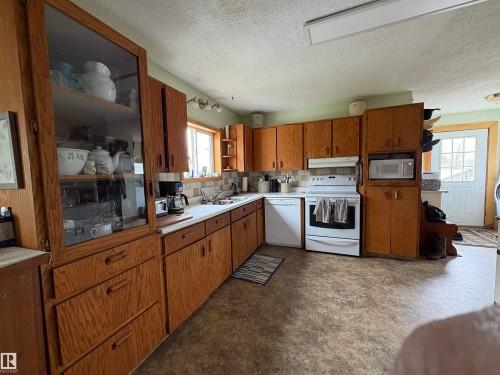 Kitchen featuring wood cabinetry, white appliances, a light-toned countertop, and a tiled backsplash. - 125 56524 Rng Rd 52A, Lindbergh, AB 