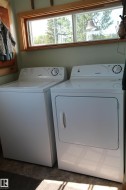 Dedicated laundry area featuring a white washing machine, white dryer, and an overhead window with natural wood trim. - 