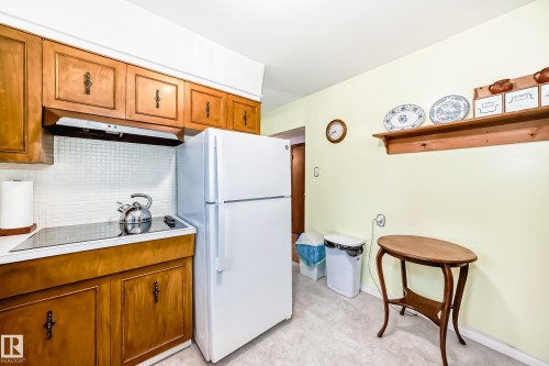 Kitchen featuring wood cabinetry, white tile backsplash, an integrated cooktop, and a white refrigerator - 8006 159 Street, Edmonton, AB 