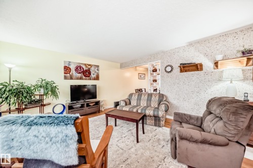 Living area featuring wood-finish flooring, a neutral wall color, patterned accent wall, and a cased opening leading to another room - 8006 159 Street, Edmonton, AB 