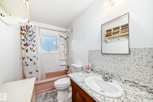 Bathroom featuring a vanity with a white oval sink, speckled countertop, and wood-finish cabinetry - 8006 159 Street, Edmonton, AB 