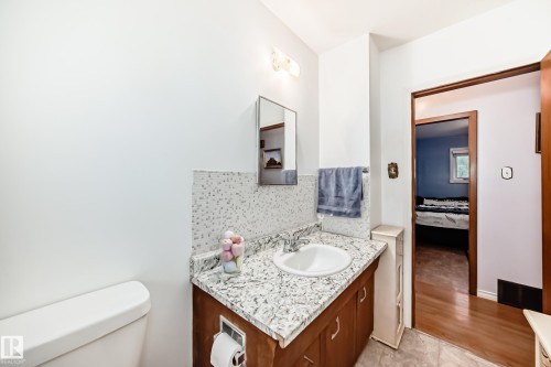 Bathroom vanity featuring a speckled countertop, integrated sink, and wood-finish cabinetry - 8006 159 Street, Edmonton, AB 