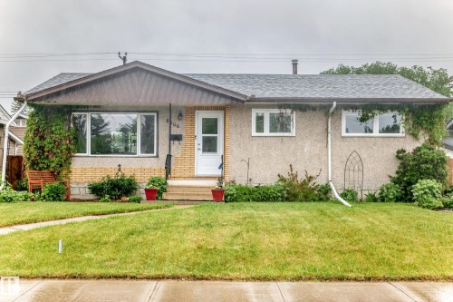 Ranch-style residence featuring a prominent front lawn with a concrete walkway, a light brick facade, and a textured stucco exterior - 8006 159 Street, Edmonton, AB 