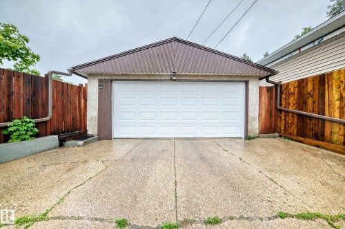 Detached garage featuring a white panel door, corrugated metal roof, and stucco exterior - 8006 159 Street, Edmonton, AB 