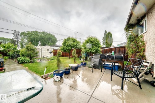 Concrete patio with direct access to a grassy yard featuring mature trees and a dedicated garden area - 8006 159 Street, Edmonton, AB 
