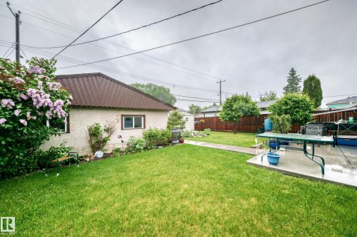 Expansive backyard featuring a manicured lawn, established shrubs, a concrete patio, and a detached structure with a brown metal roof - 8006 159 Street, Edmonton, AB 