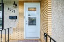 Entryway featuring a white door with upper glass panels, light-toned brick accents, textured stucco siding, and black metal handrails - 8006 159 Street, Edmonton, AB 