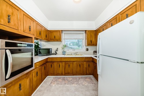 U-shaped kitchen featuring wood cabinetry, white countertops, a stainless steel built-in oven, and a white refrigerator - 8006 159 Street, Edmonton, AB 