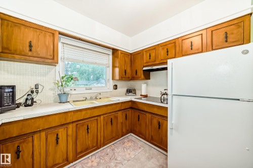 Kitchen featuring wood cabinetry, white countertops, tile backsplash, and a double basin sink - 8006 159 Street, Edmonton, AB 