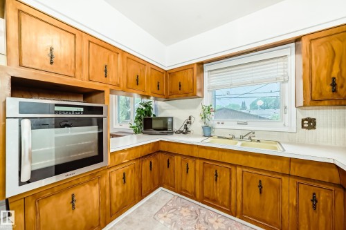 Kitchen featuring wood cabinetry, white countertops, a built-in wall oven, a double basin sink, and a window with blinds - 8006 159 Street, Edmonton, AB 