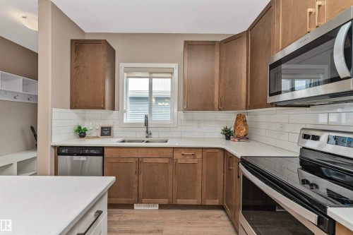 Kitchen featuring wood-finish cabinetry, white countertops, subway tile backsplash, and stainless steel appliances including a dishwasher, microwave, and electric range - 22124 85 Avenue, Edmonton, AB - Indoor Photo Showing Kitchen With Stainless Steel Kitchen With Double Sink