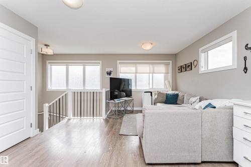 Spacious open-concept area featuring wood-finish flooring, multiple windows with roller shades, a contemporary white interior door, and a staircase with white railings - 22124 85 Avenue, Edmonton, AB - Indoor