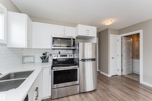 Kitchen featuring white cabinetry, stainless steel appliances, white subway tile backsplash, white countertops, and wood-finish flooring - 22124 85 Avenue, Edmonton, AB - Indoor Photo Showing Kitchen With Stainless Steel Kitchen With Double Sink