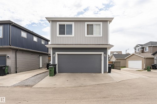 Two-story exterior with light gray vertical siding and horizontal dark gray siding, featuring a dark gray garage door, white framed windows, and a concrete driveway - 22124 85 Avenue, Edmonton, AB - Outdoor