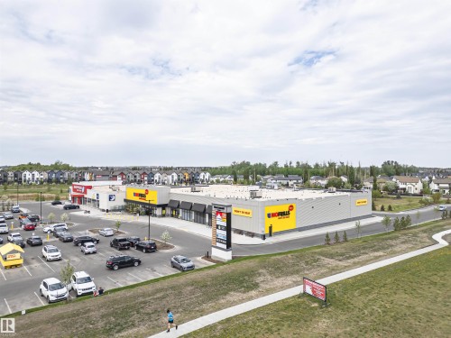 Commercial retail center featuring a large asphalt parking lot, multiple storefronts with black awnings, and prominent signage - 22124 85 Avenue, Edmonton, AB - Outdoor With View