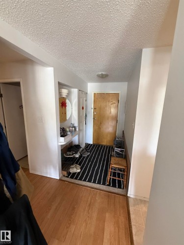Entryway featuring wood-finish flooring transitioning to tile, a built-in shelving unit, a textured ceiling, and a flush-mount ceiling light - 225 4404 122 Street, Edmonton, AB 