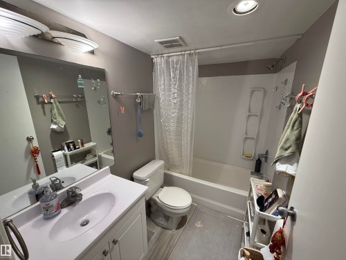 Bathroom featuring a white vanity with an integrated sink, a rectangular mirror, a toilet, and a shower-tub combination with a white surround - 225 4404 122 Street, Edmonton, AB 