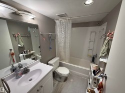 Bathroom featuring a white vanity with an integrated sink, a rectangular mirror, a toilet, and a shower-tub combination with a white surround - 