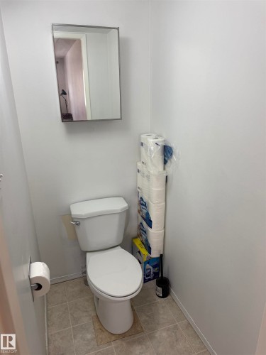 White ceramic toilet with a wall-mounted mirror above, set on neutral-toned tiled flooring - 225 4404 122 Street, Edmonton, AB 
