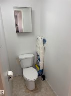 White ceramic toilet with a wall-mounted mirror above, set on neutral-toned tiled flooring - 