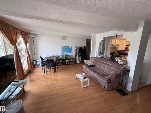 Open-concept living space featuring wood-finish flooring, white walls, and a sliding glass door - 225 4404 122 Street, Edmonton, AB 