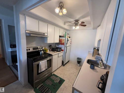 Galley kitchen featuring white cabinetry, light-toned countertops, and a stainless steel oven with an overhead microwave hood - 225 4404 122 Street, Edmonton, AB 