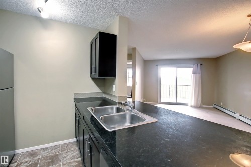 Kitchen featuring dark cabinetry, dark countertops, a double stainless steel sink, and tile flooring - 215 1510 Watt Drive, Edmonton, AB 