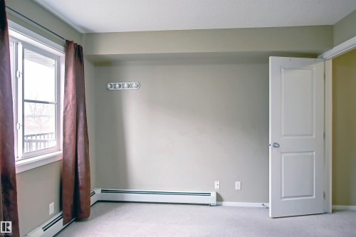 Neutral-toned room featuring a double-hung window, light-colored carpeting, baseboard heaters, and a white interior door - 215 1510 Watt Drive, Edmonton, AB 