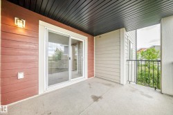 Covered concrete balcony featuring a sliding glass door, exterior wall lighting fixture, and black metal railing - 