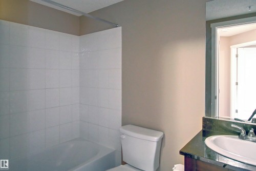 Bathroom featuring a white tiled shower and tub combination, a toilet, and a vanity with a dark countertop and an undermount sink - 215 1510 Watt Drive, Edmonton, AB 