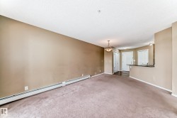 Spacious living area featuring neutral-toned walls, textured ceiling, and baseboard heating - 