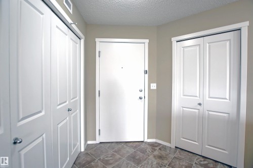 Entryway featuring a white paneled door, two white bifold closet doors, and patterned tile flooring - 215 1510 Watt Drive, Edmonton, AB 