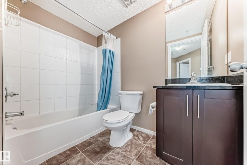 Bathroom featuring a dark wood-finish vanity with a dark stone countertop, undermount sink, and chrome faucet - 215 1510 Watt Drive, Edmonton, AB 