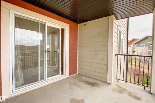 Covered concrete balcony featuring a sliding glass door, black metal railing, and horizontal siding - 215 1510 Watt Drive, Edmonton, AB 