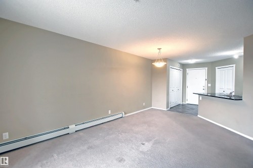 Open-concept living area featuring neutral wall tones, textured ceiling, and gray carpet flooring - 215 1510 Watt Drive, Edmonton, AB 