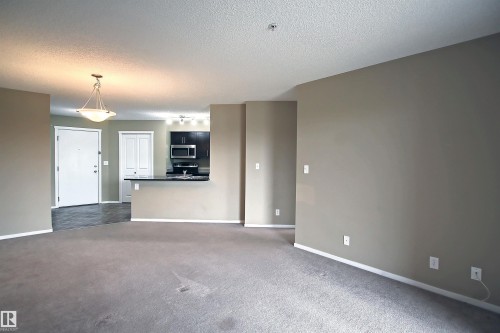 Carpeted living space featuring neutral wall tones, white baseboards, and a pendant light fixture - 215 1510 Watt Drive, Edmonton, AB 