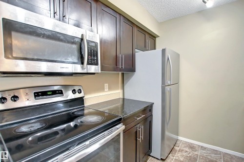 Kitchen featuring dark wood cabinetry, a built-in stainless steel microwave, and a black electric range with a glass cooktop - 215 1510 Watt Drive, Edmonton, AB 