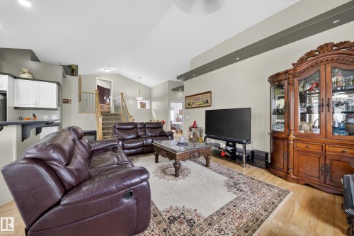 Open-concept living space featuring vaulted ceilings, light wood-finish flooring, a breakfast bar with white cabinetry, and a staircase with wood railings and carpeted treads - 4113 59 Street, Beaumont, AB 