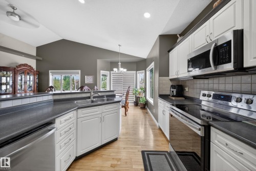 Kitchen featuring white cabinetry, stainless steel appliances, a tile backsplash, dark countertops, and wood-finish flooring - 4113 59 Street, Beaumont, AB 