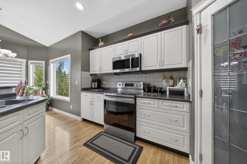 Kitchen featuring light wood-finish flooring, white cabinetry with dark trim, stainless steel appliances, a tile backsplash, and multiple windows - 4113 59 Street, Beaumont, AB 