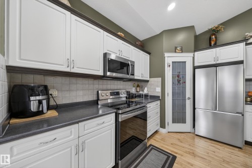 Kitchen featuring white cabinetry with dark crown molding, stainless steel appliances, light wood-finish flooring, and a tiled backsplash - 4113 59 Street, Beaumont, AB 